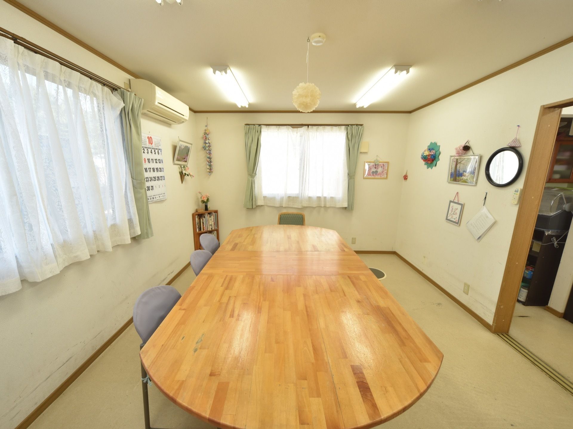 空調を完備し、２面に窓のある談話室。絵画や手芸作品などが壁に掲示されている。大きなテーブルに椅子が数脚置かれている。