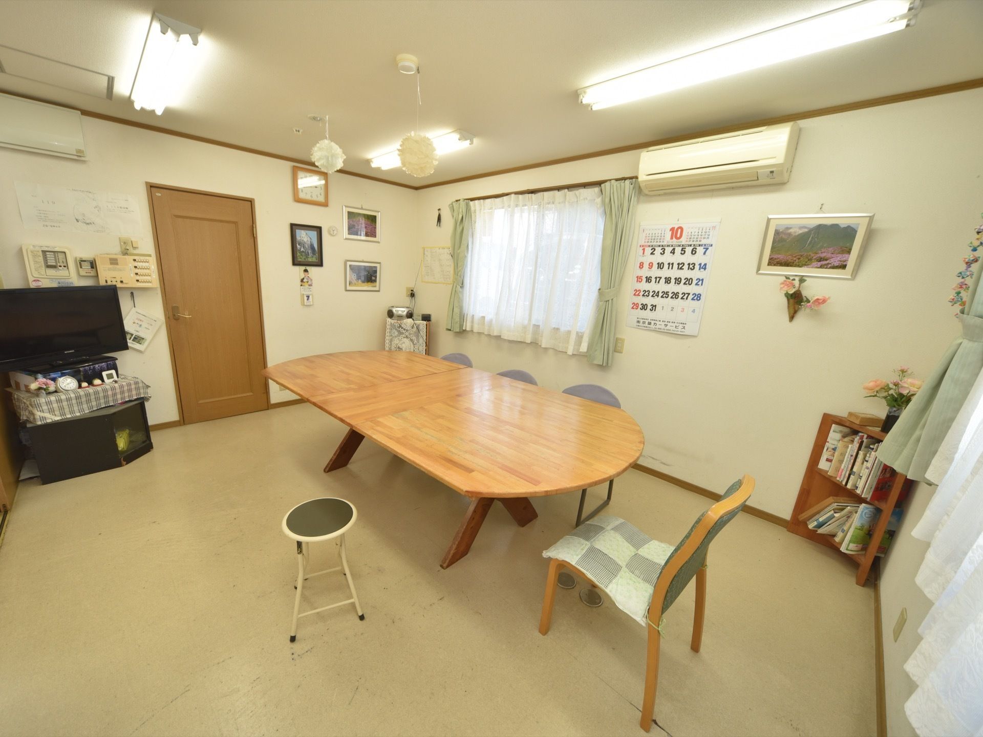 談話室の壁にはカレンダーがあり、時計がかけられている。また室内には風景写真があり、造花も飾られている。