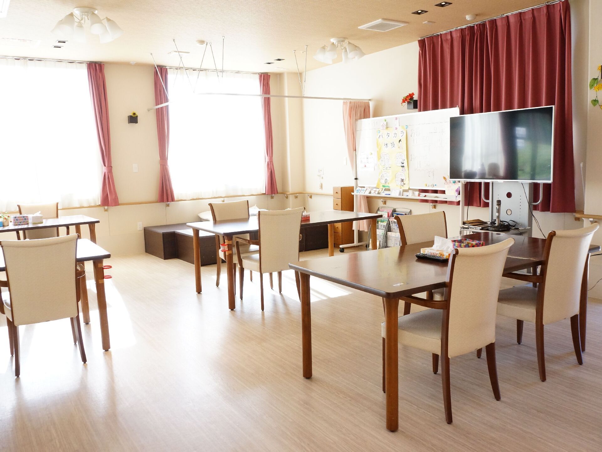テーブルが並び、大型のテレビが設置され、大きな窓がある食堂