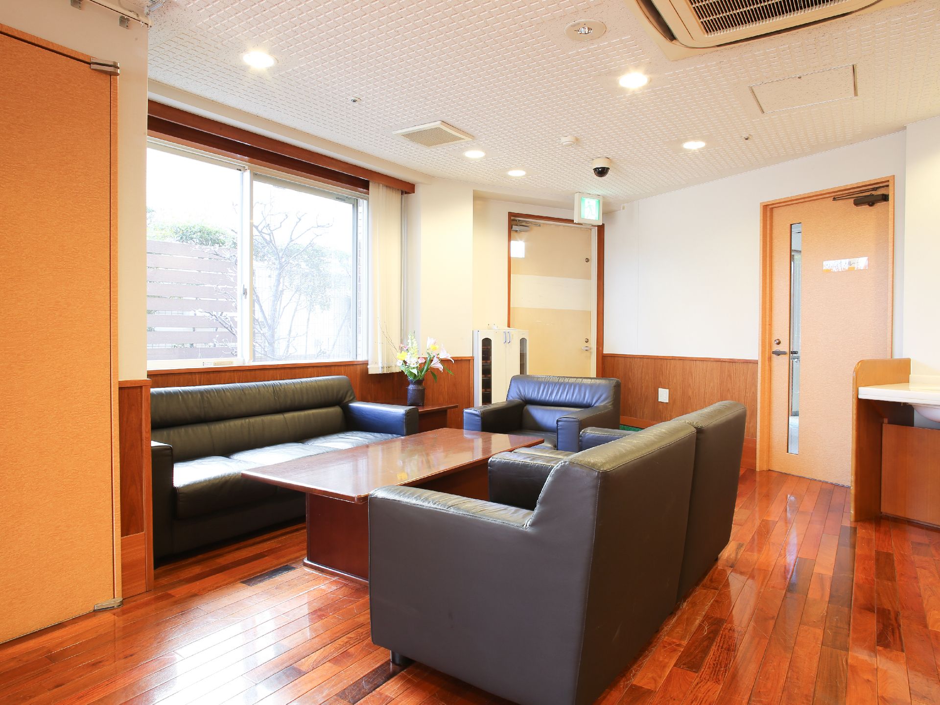 部屋におかれた長テーブルを囲うように革張りのソファーが設置されている。角には花瓶に差した花が飾られている。