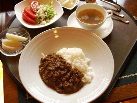 黒いお盆の上に、カレーライス、スープ、サラダ、果物が並べられている。フォークやスプーンが用意されている。