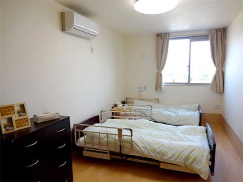 エアコン、引き出しが設置され、介護ベッドが２つ並んだ２人部屋