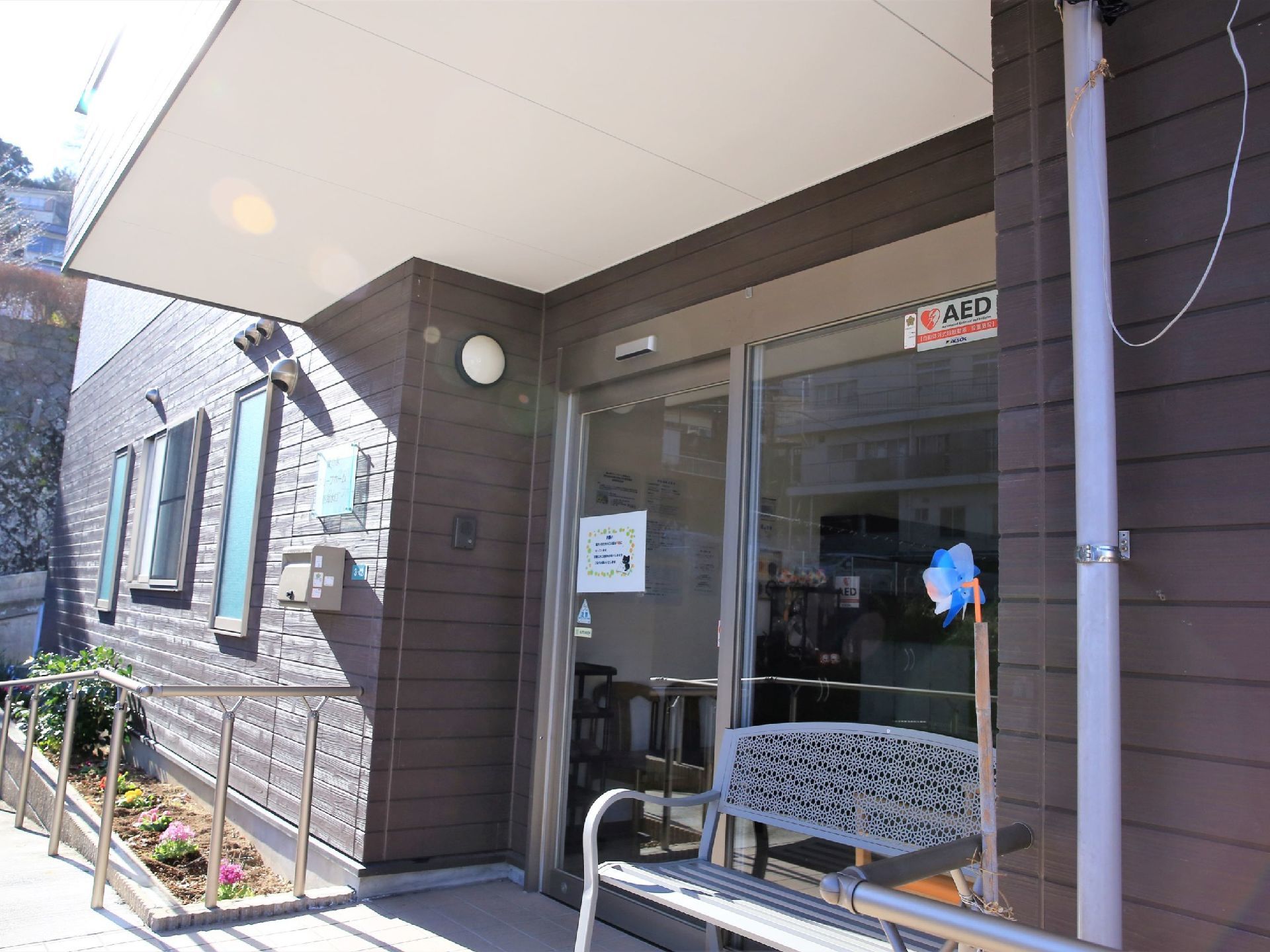 屋根付きの玄関で、横には花壇が設置されている。自動ドア前の外壁には、照明とインターホンが取りつけられている。