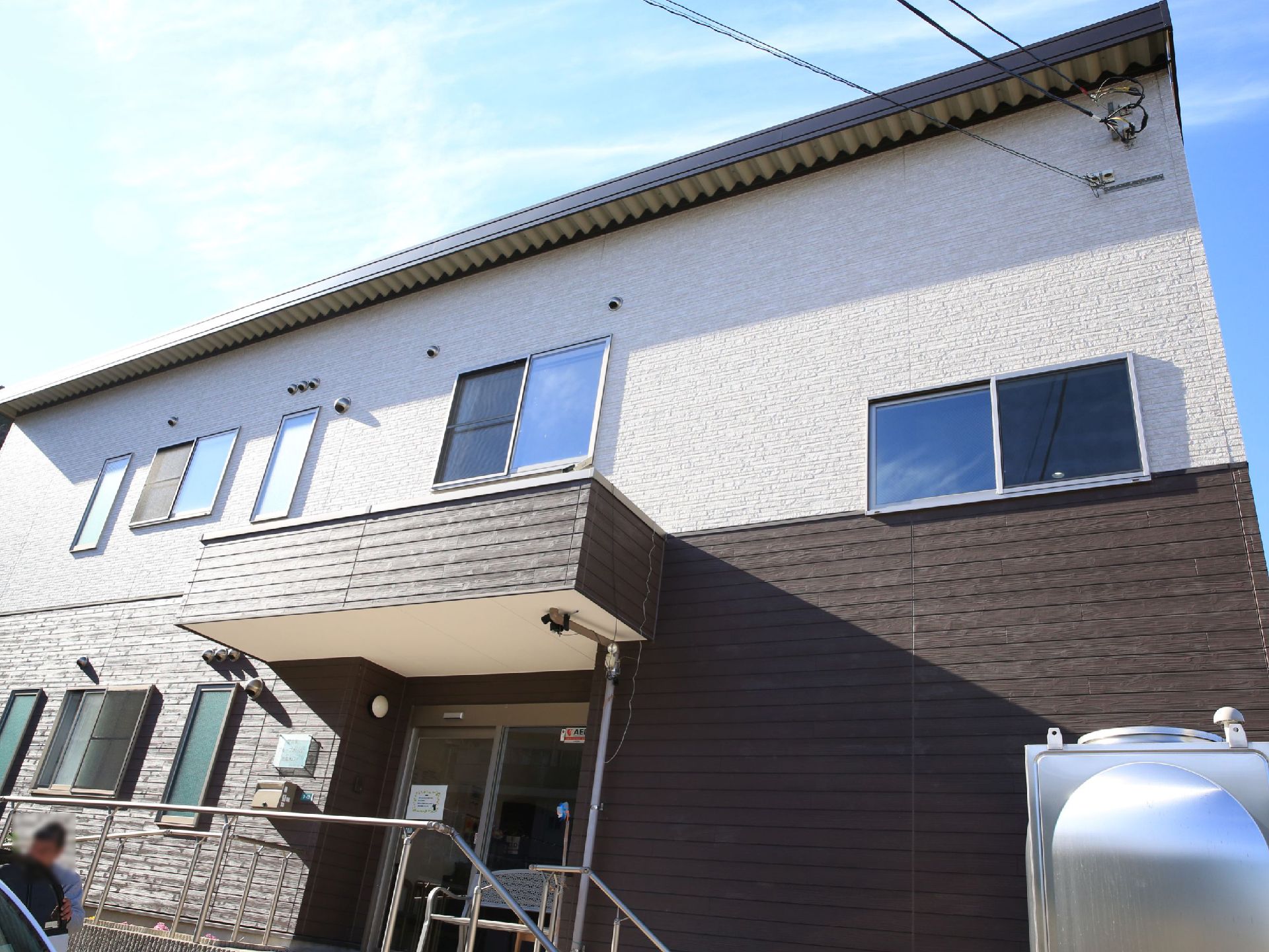 ブラウンを基調とした落ち着いた色合いの２階建てのグループホーム。施設目の前には駐車場が設けられている。