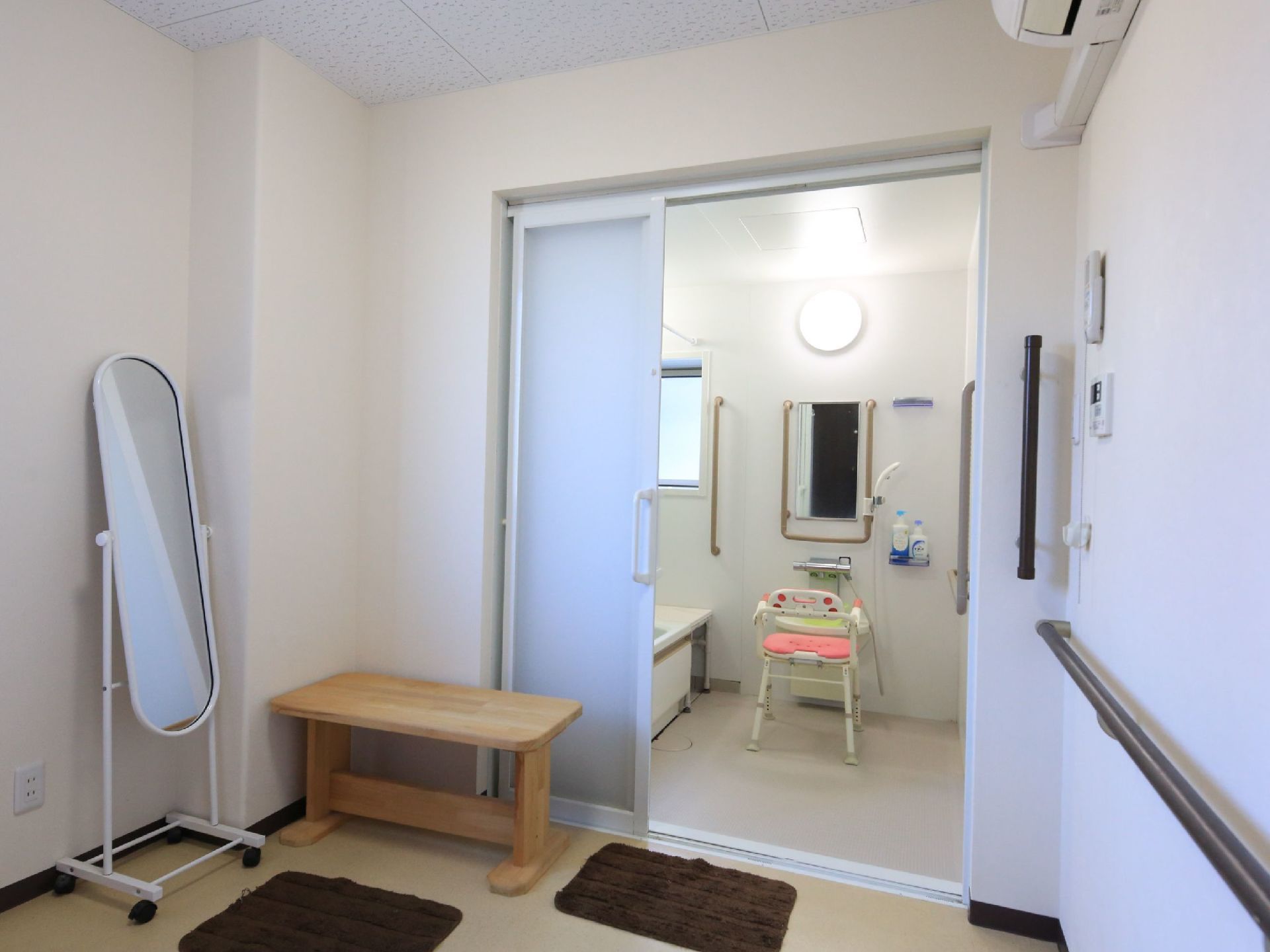 清潔感のある脱衣所には、ベンチやキャスター付きの全身鏡が設置されている。床には足拭きマットが敷かれている。