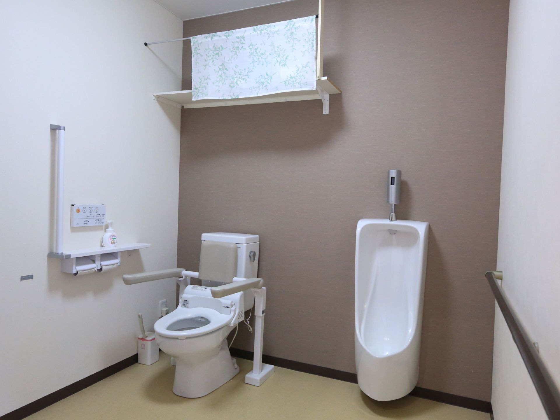 バリアフリー仕様のゆとりある共用のトイレで、洋式とストール型の便器が並べて設置されている。上部には収納棚が取りつけられている。
