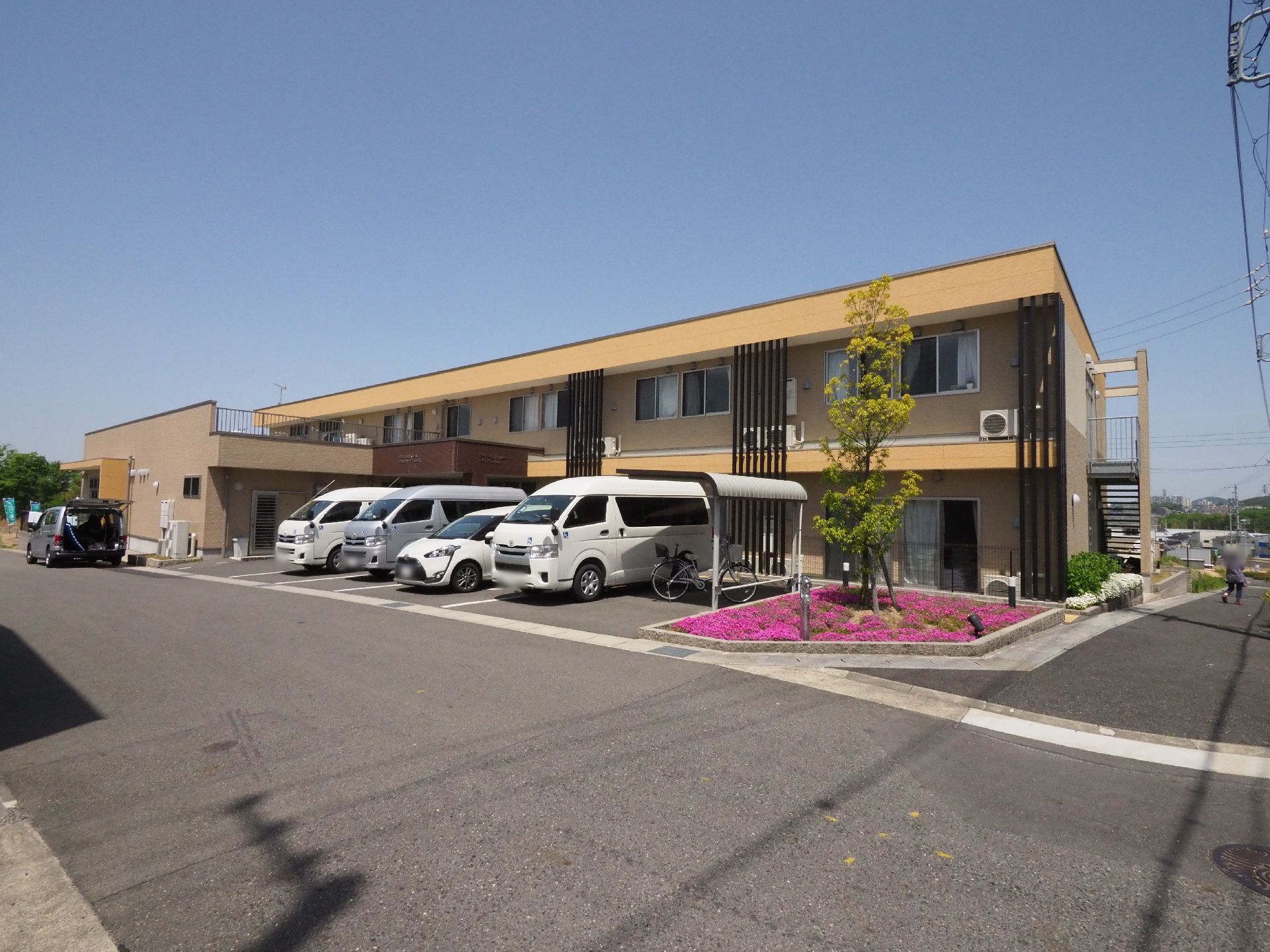 敷地内に駐車場を設けている。花の咲く花壇が美しい施設の外観。