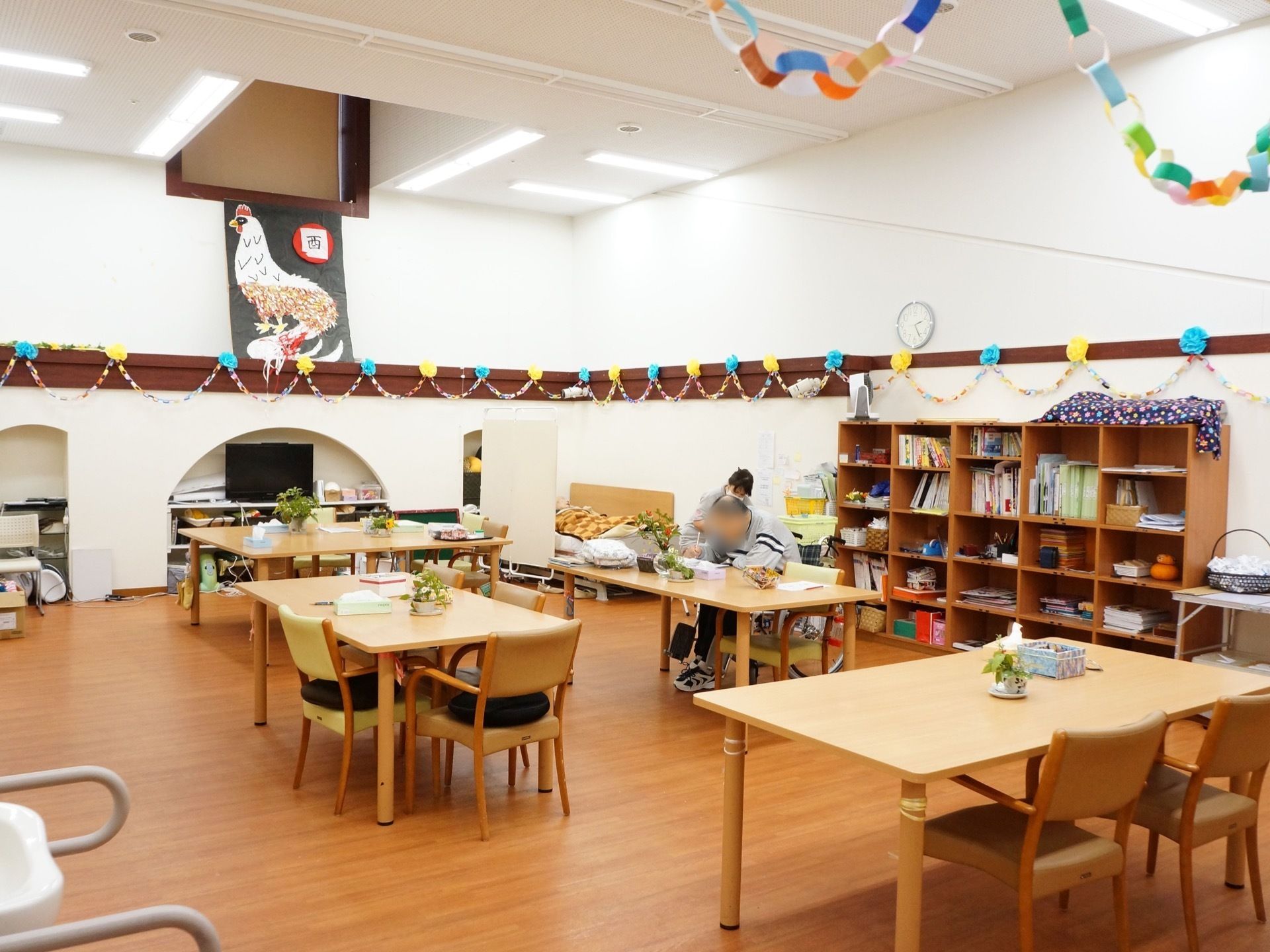 広々とした共用スペースには、たくさんのイスやテーブルが置かれている。またフロアには介護用ベッドも置かれている。