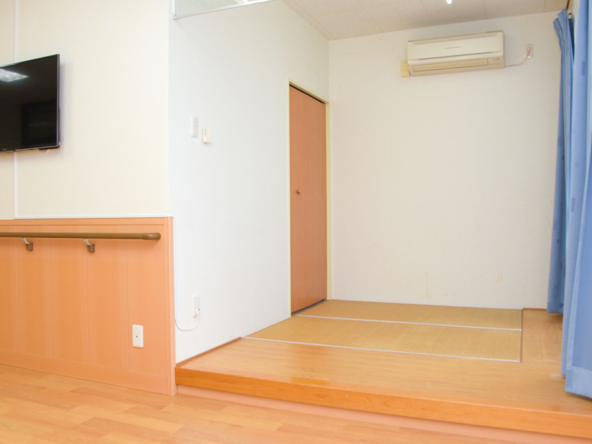 室内にはエアコンが一台壁に取り付けてある。青色のカーテンが取り付けてある。テレビが一台壁に取り付けてある。