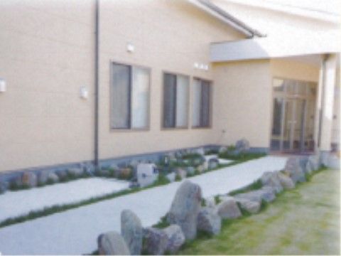 自動ドアを出てくると、散歩をすることができる通路がある。大きな石が並べられている。クリーム色の建物の壁には窓がある。
