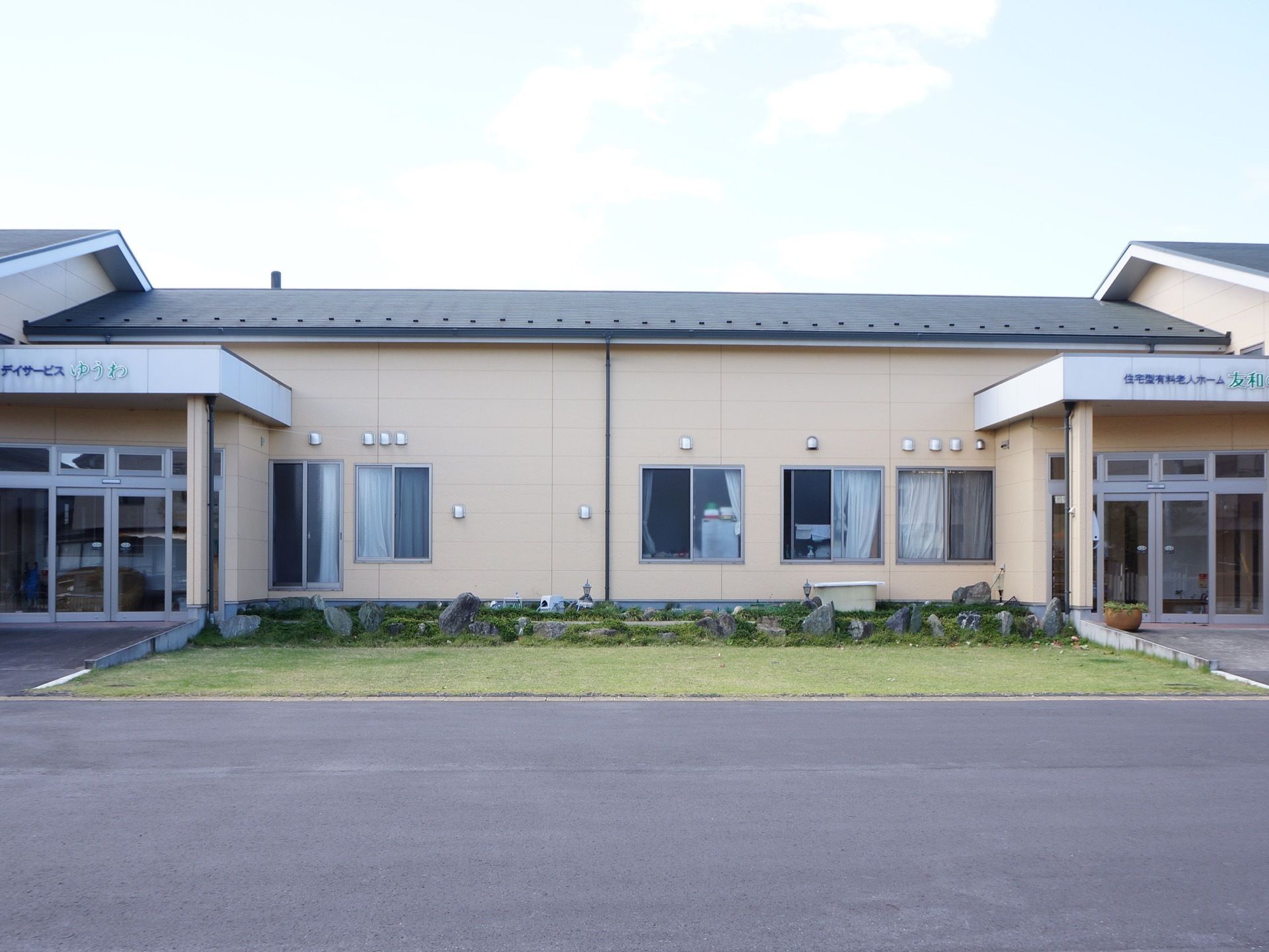 ピンク系の温かみを感じる平屋建ての施設である。エントランス周辺は段差がないので安全に通行できる。手入れの行き届いた庭がある。
