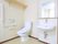 居室内に設置されたトイレの図である。中央に温水洗浄便座があり、壁に操作パネルと非常ボタンが取り付けられている。