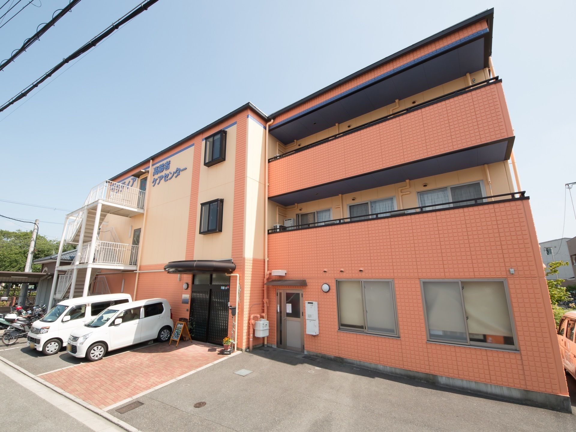 ピンクとクリーム色の外観で柔らかい印象があり、駐車スペースが広い。窓にはカーテンやロールスクリーンを設置しプライバシーにも配慮している。
