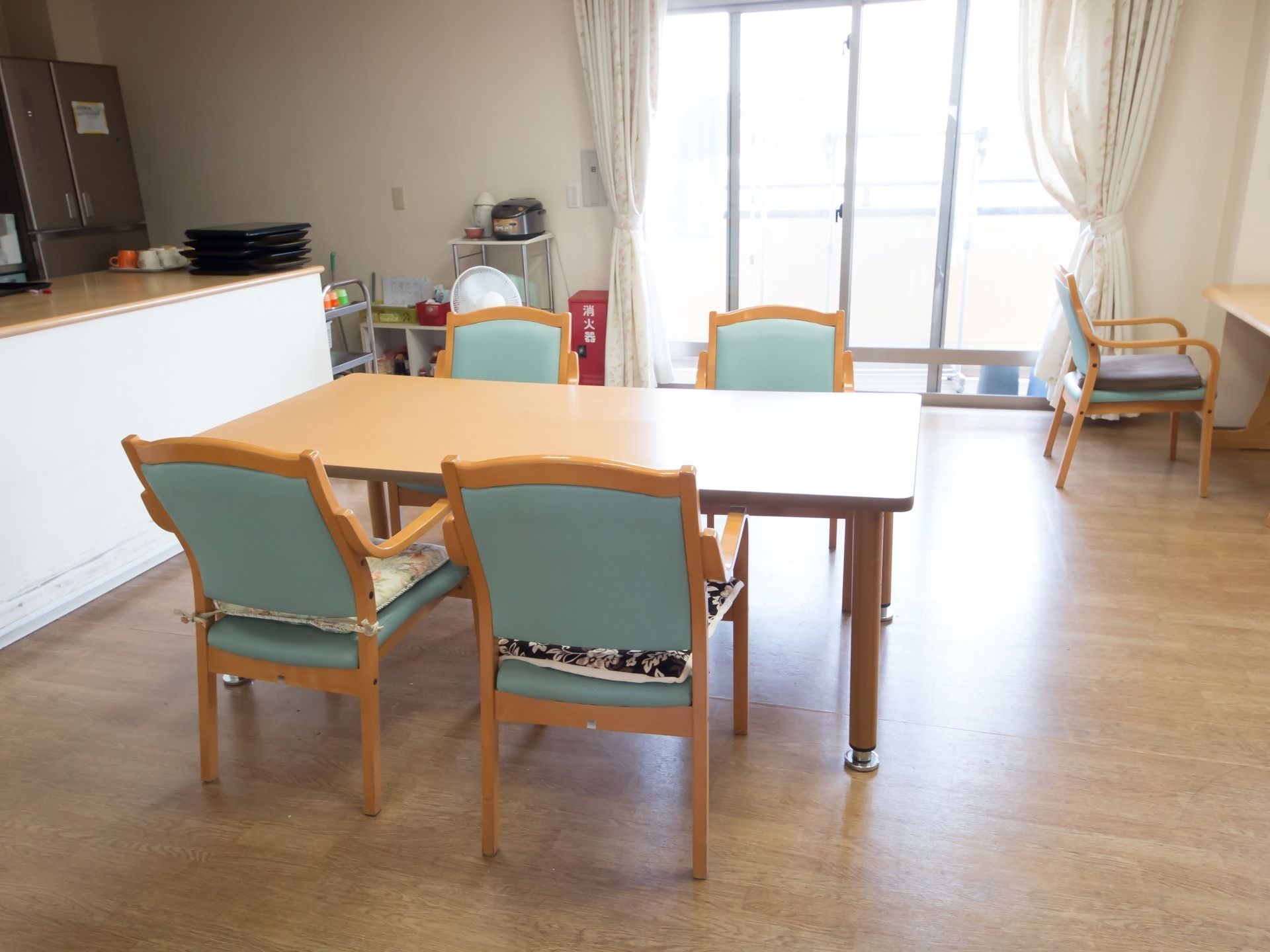 4人でテーブルを囲める配置にしていて椅子にクッションを置いている。カウンターキッチンでスタッフが様子を確認しやすい。