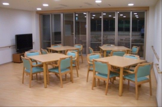 天井につけられた多くのダウンライトが明るく照らす食堂。4人掛けのテーブルが数多く置かれ、壁際には大型テレビも設置されている。