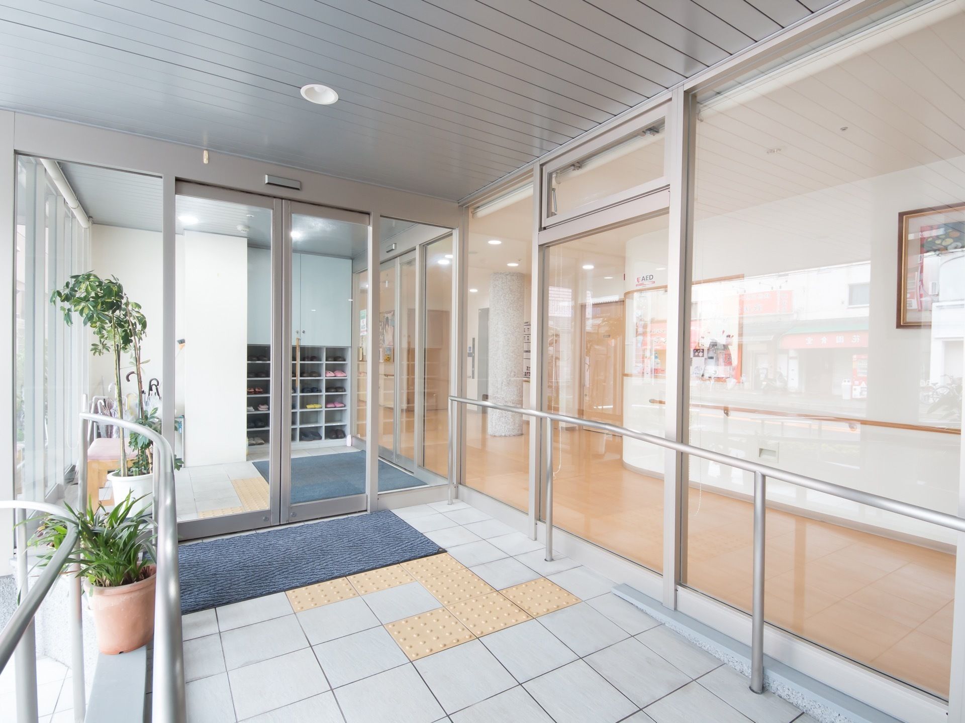 玄関を建物内から写した様子。玄関を入るとすぐに点字ブロックが設置されている。手すりも完備されていて、安全面での配慮がある。