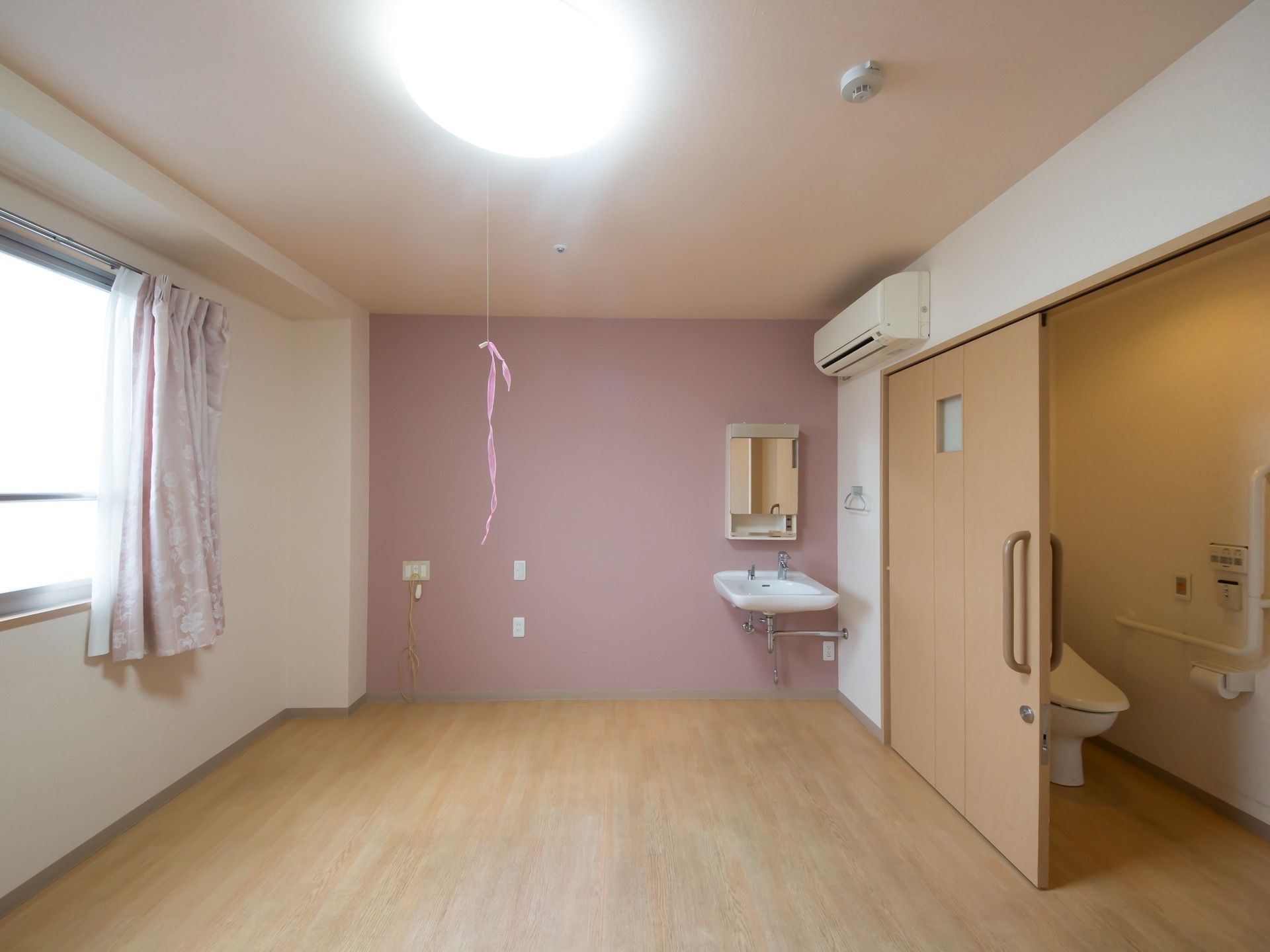 居室内に広々とした清潔なトイレがある。壁には手すりがついているため、安心してご利用いただける。トイレを出るとすぐに洗面台もある。