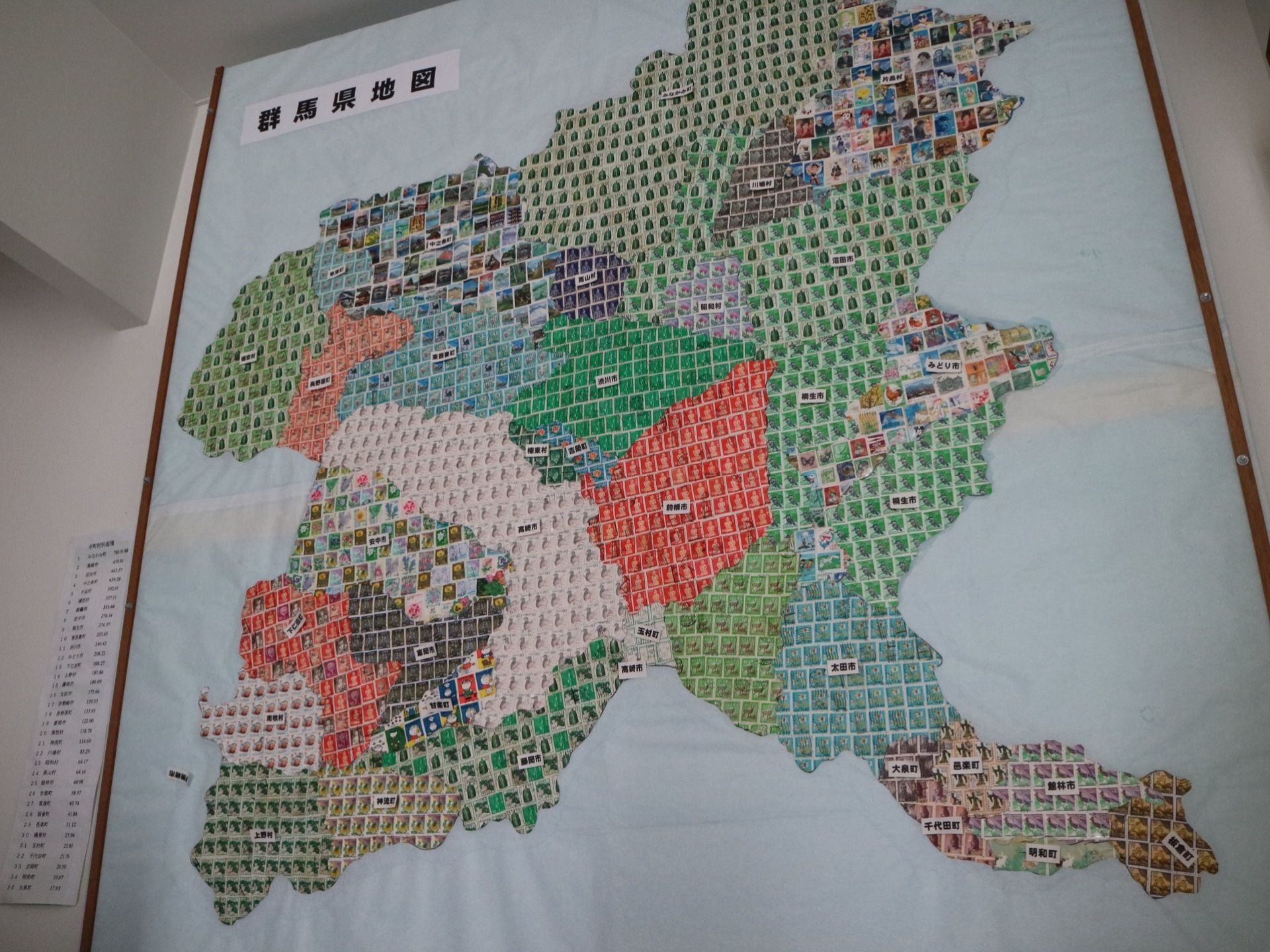古切手を敷き詰めて貼り合わせて作った群馬県の地図である。都市ごとに切手の種類や色を変えており、市町村名が示されている。