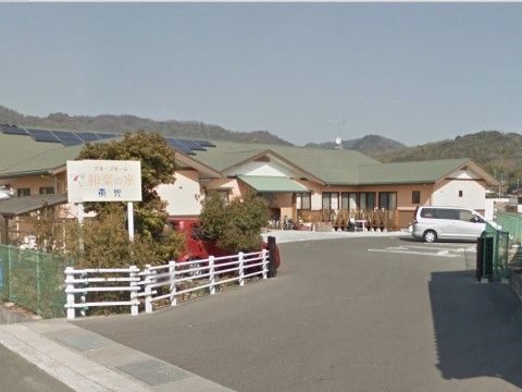 山々に囲まれ自然豊かな環境に建つ建物。緑色の屋根と淡いオレンジ色の壁が周囲の景色に溶け込む。敷地内には広い駐車場が完備されている。