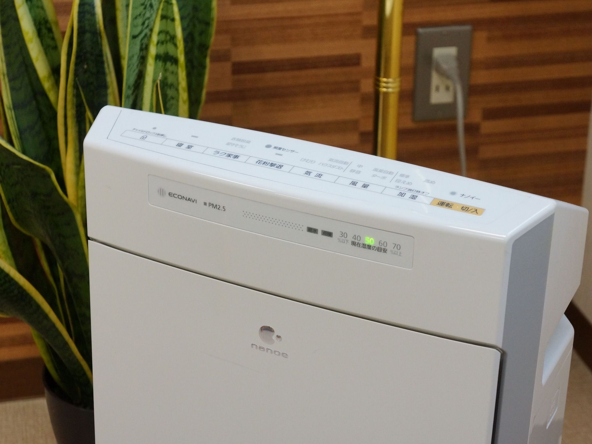 PM２．５にも対応している空気清浄機で、湿度の目安が表示される。加湿機能も付いている。後ろには、観葉植物が置かれている。