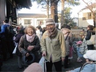 周囲にたくさんの人々がいる中、2人の入居者様が並んで笑顔で写真を撮っている。周辺には住宅街が広がっている。