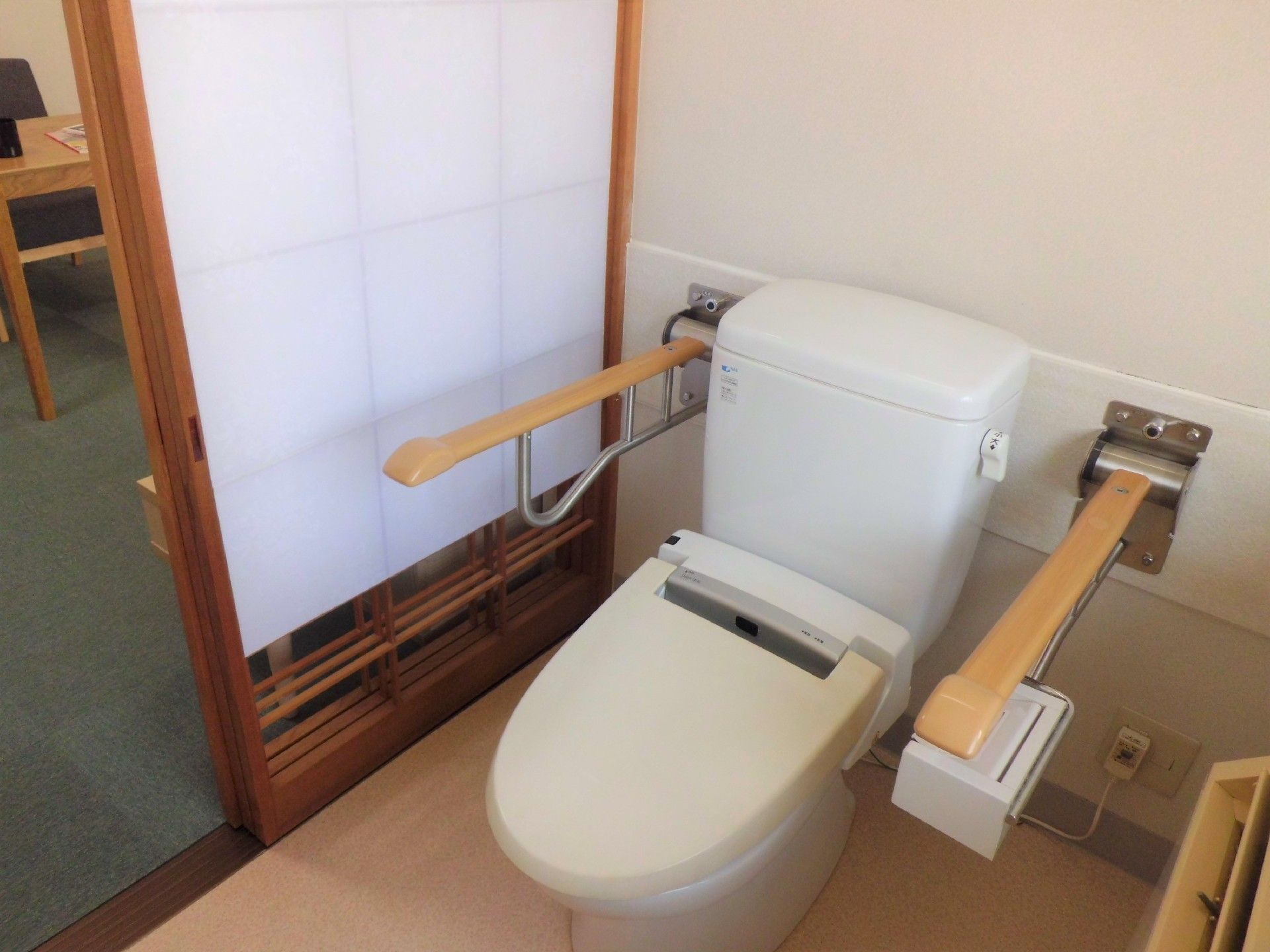 手すりが両サイドに設置されたシンプルな様式のトイレ。トイレの出入り口には障子が設置されている。