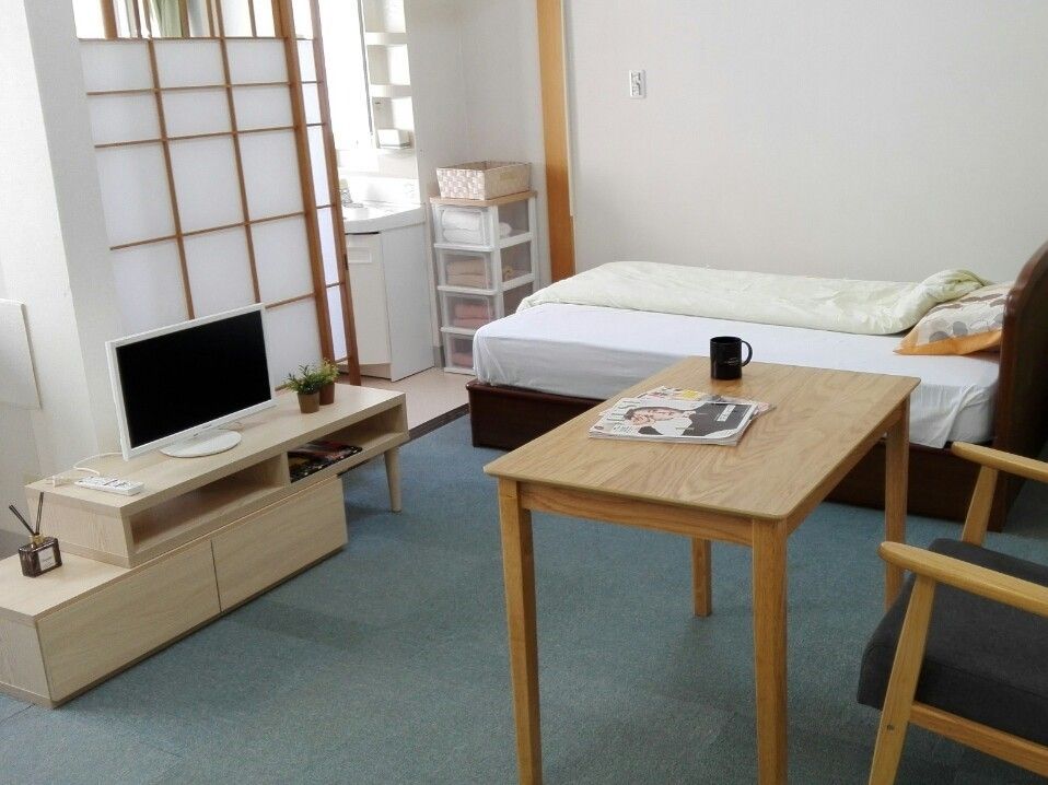 テレビラックの前には木製のテーブルやいすが置かれ、奥には寝具がセットされたベッドがある。