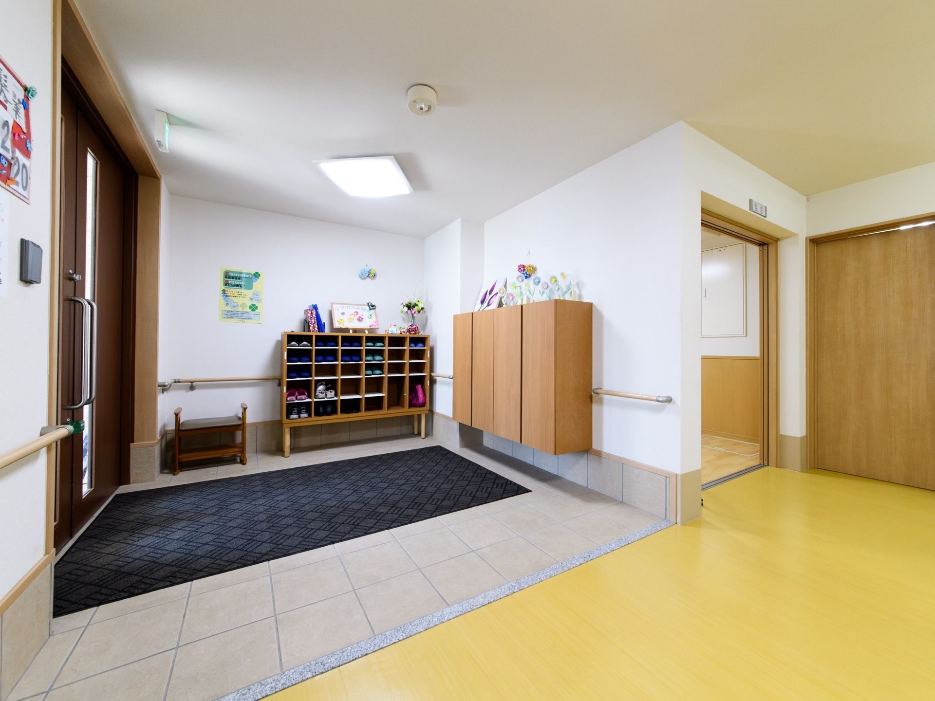 靴箱の横に１人掛けのベンチが置かれている。靴の履き替えの際に使用ができる。靴箱の上にはさまざまな作品が飾られている。