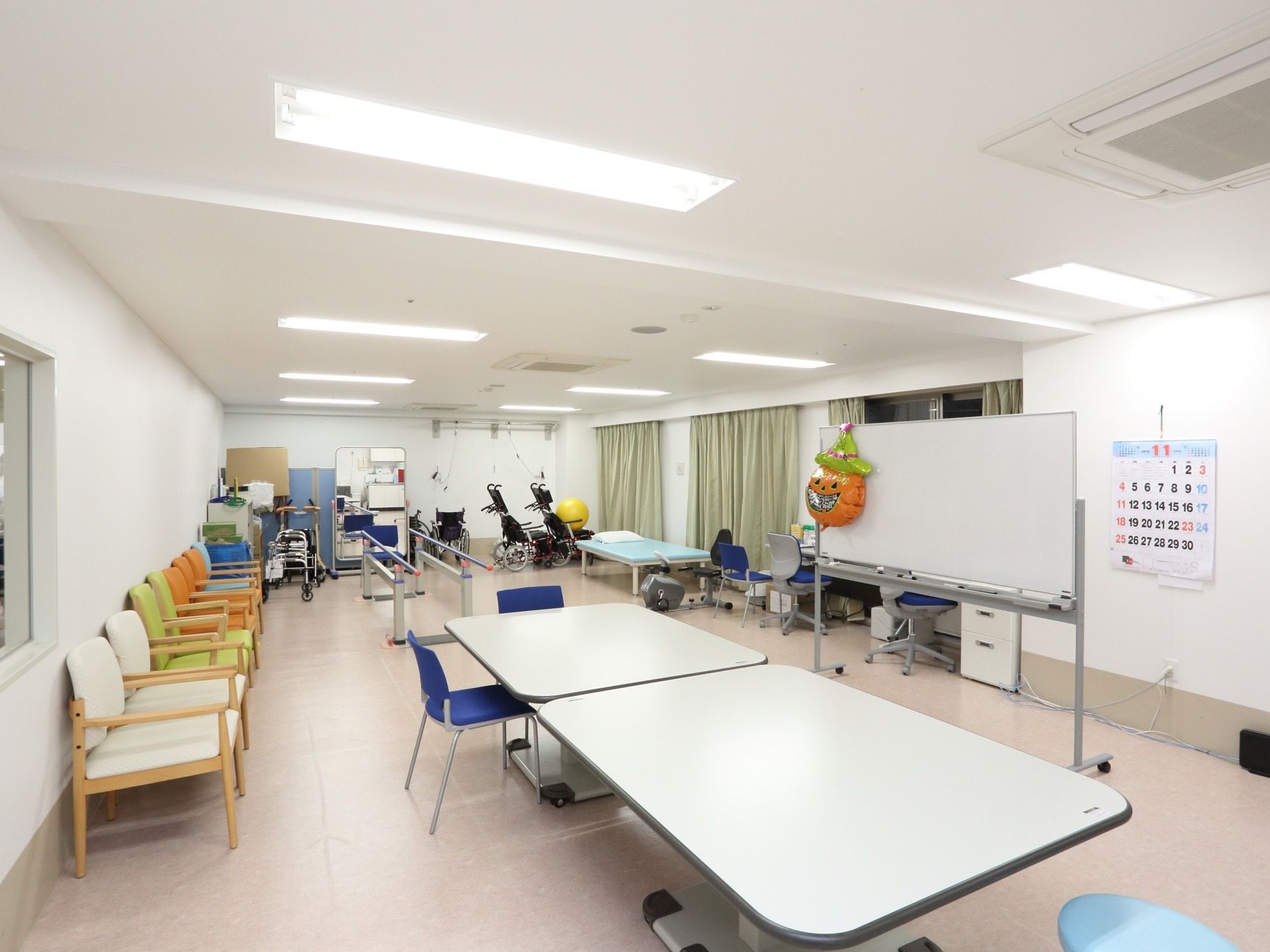 機能訓練室は広いスペースで、運動機器やベッドが置かれている。デスクやホワイトボードも置かれ、リハビリの説明もできるようになっている。