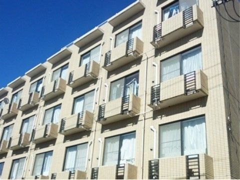 青空の下、ベージュ色で部屋ごとにベランダの付いた外観の建物
