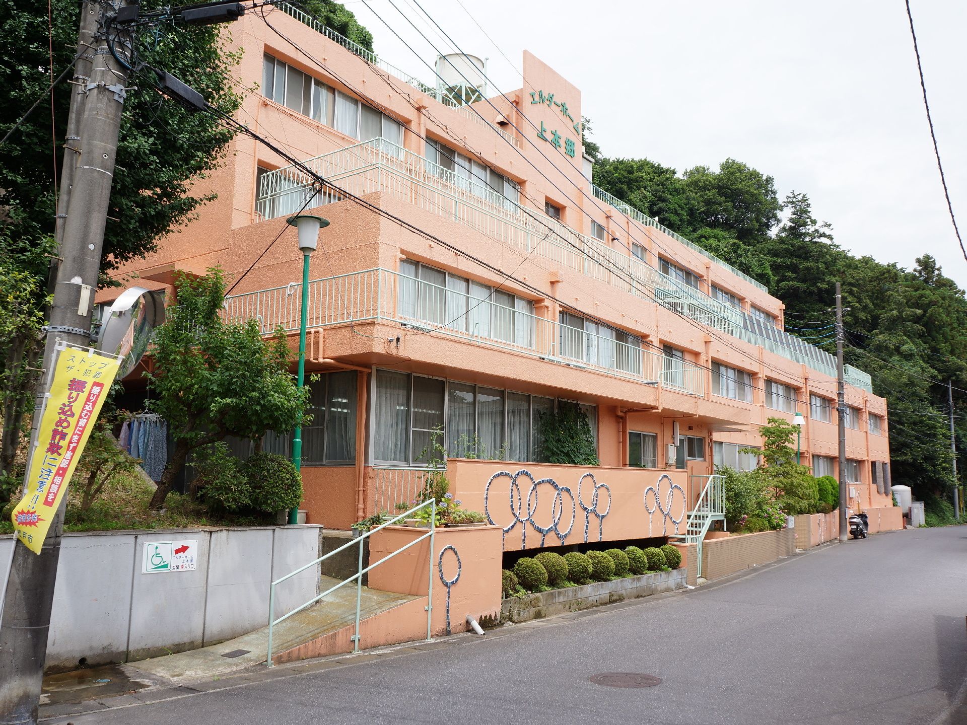 緑の木々に囲まれて建つ建物は、暖かな色合いの外壁が特徴的な4階建て。建物の横にはスロープが用意されている。