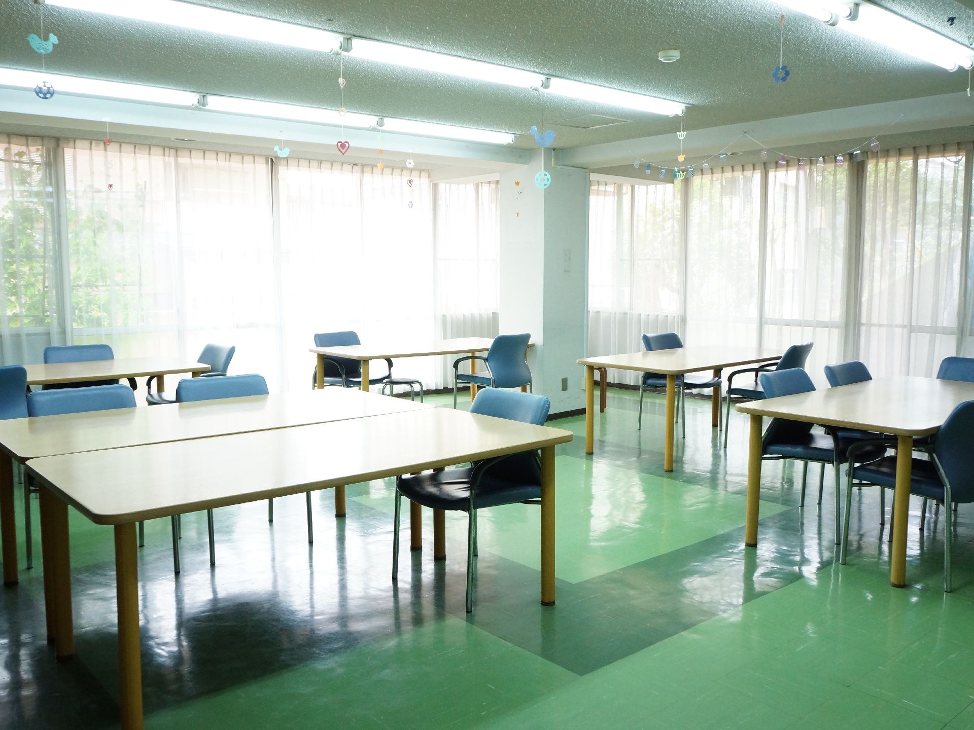 食堂の壁は一面大きな窓になっていて、日中は日の光が降り注ぐ開放的な空間。緑の床と天井から下げられたリースが特徴。