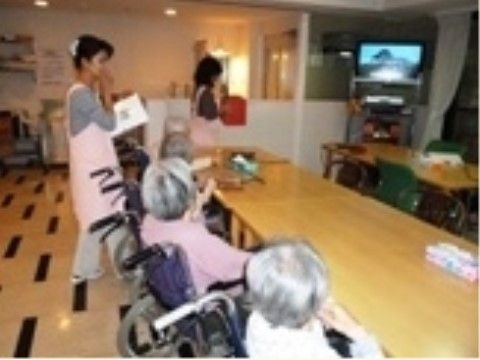 テーブルに向って座っている車椅子を利用する数人の高齢者と会話しているエプロンをかけた女性