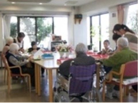 大きなテーブルを囲んで、車椅子や椅子に腰を掛けて食事をしている高齢者とそれを介助する職員