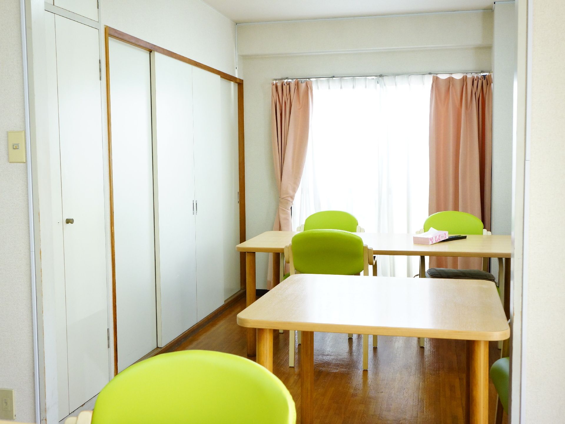 ダイニングテーブルや椅子が並べられた奥には大きな窓があり、明るい陽の光が部屋を照らしている。テーブルにはティッシュが置かれている。
