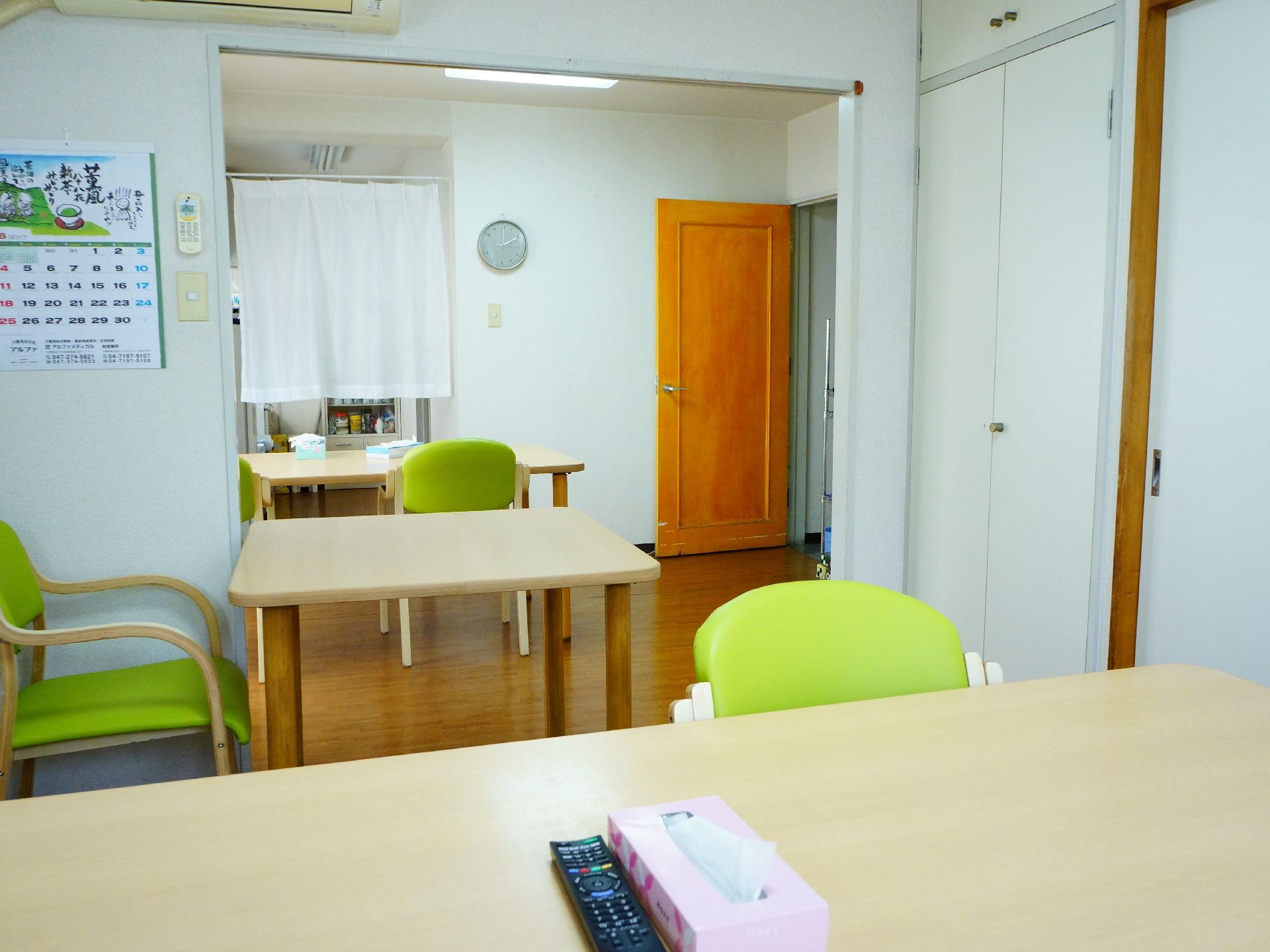 部屋に並べられたテーブルの上には箱ティッシュやテレビのリモコンが置かれている。奥の部屋との境には暖簾がかけられている。