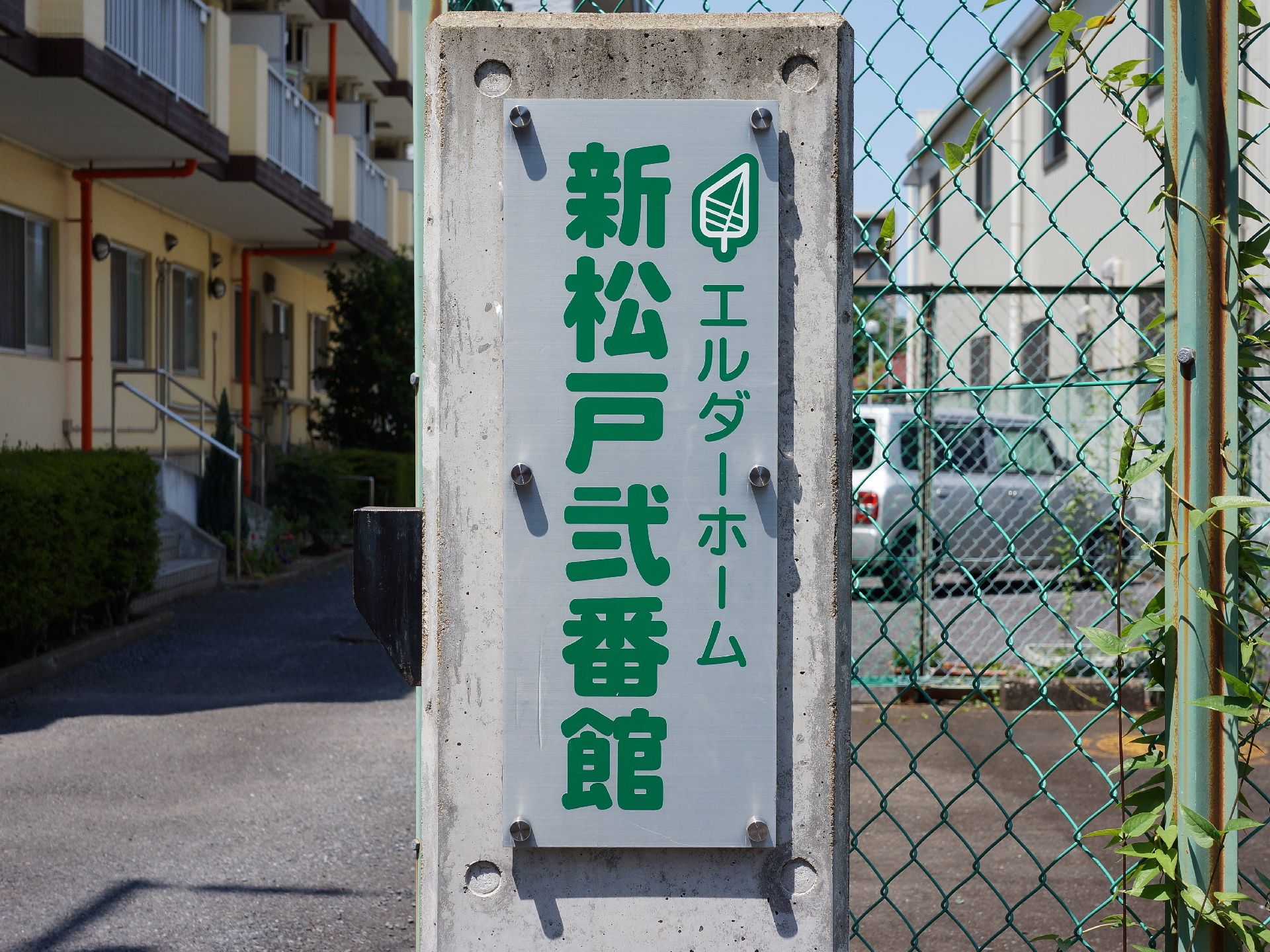 施設の入り口には、白地にグリーンの大きな文字で施設名が表示されているパネルがある。コンクリートの柱に取り付けられている。