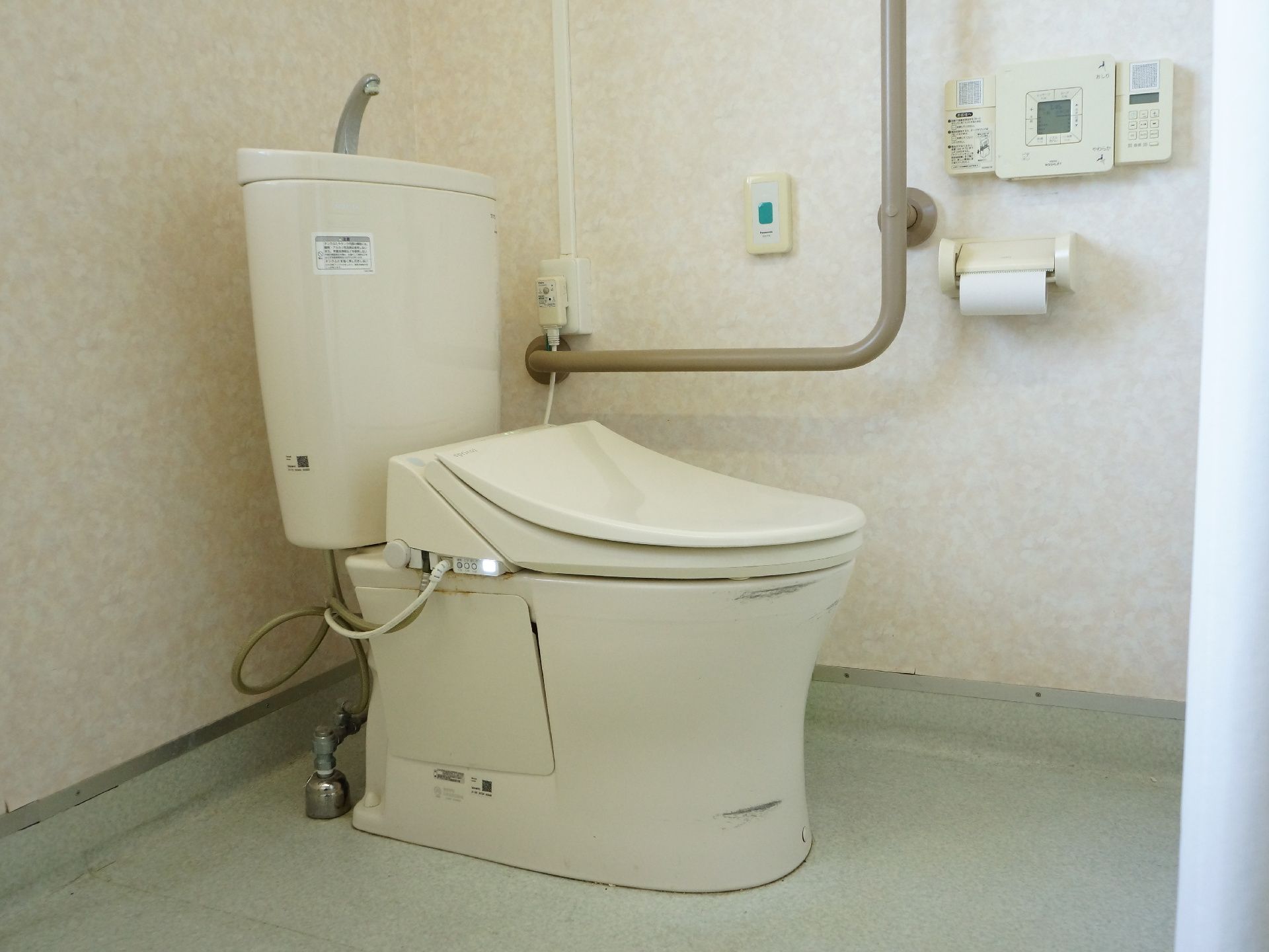 フロアの角部分にトイレが設置されている。左側の壁には立ち動作をサポートする手すり、ナースコール、操作パネルがある。