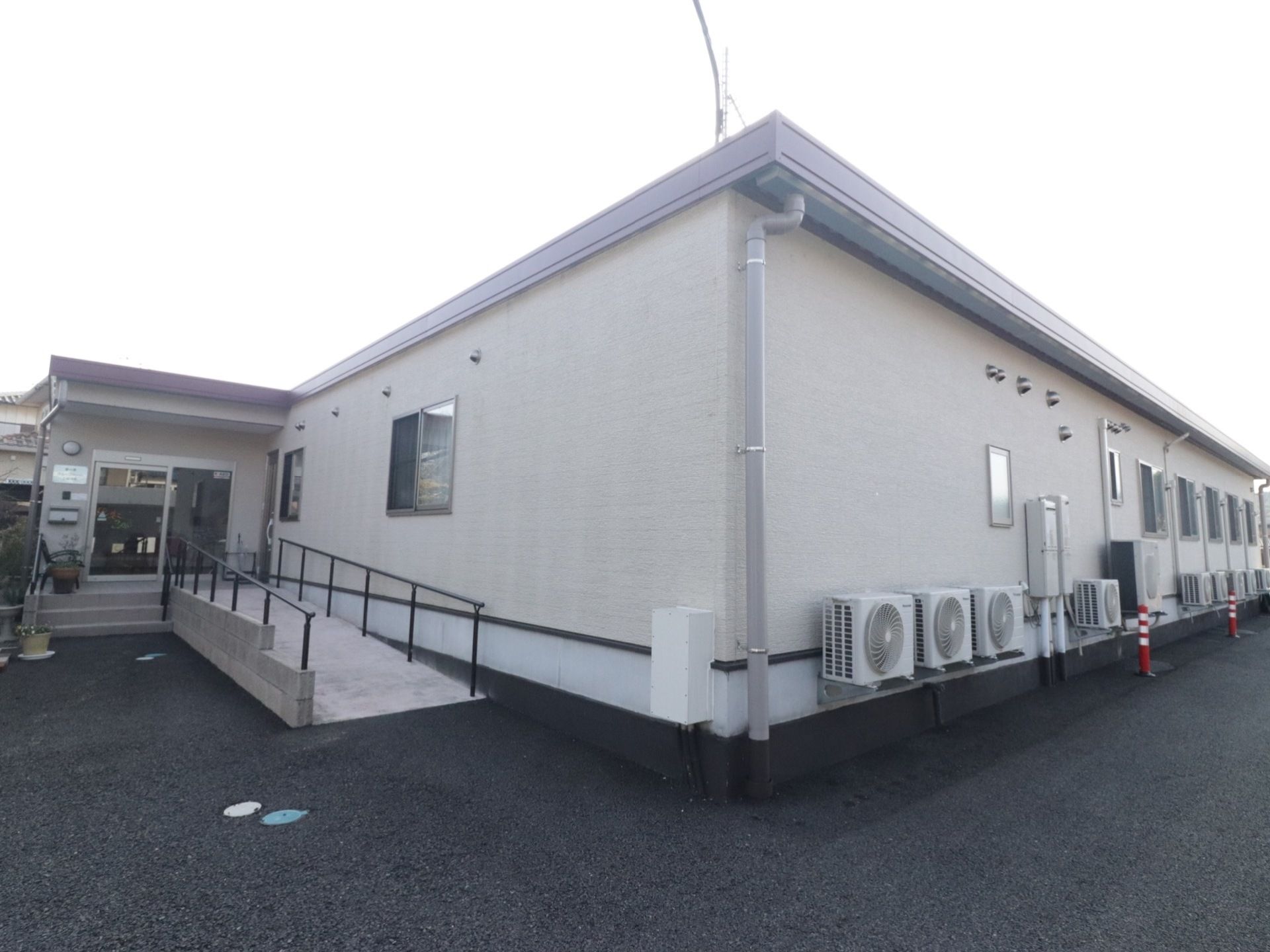 建物は１階建てである。右手の外壁の室外機がいくつも取り付けられている。左手に玄関に続くスロープがある。