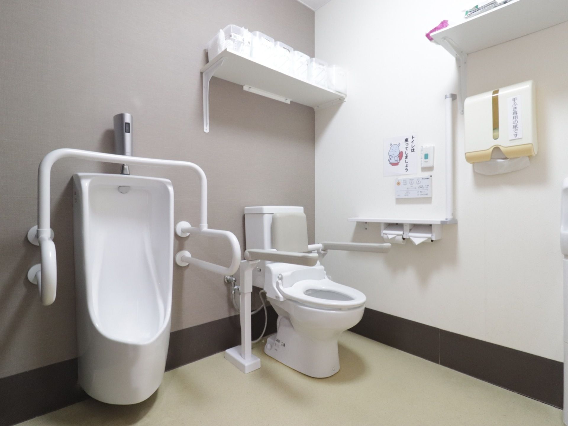 トイレの個室内に、温水洗浄便座付き便器と、男性用便器がある。トイレには手すりが付いていて、壁には呼出ボタンがある。