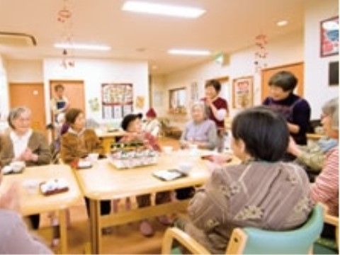 テーブルを囲んで座っている高齢者の右側で、立って話をしている女性