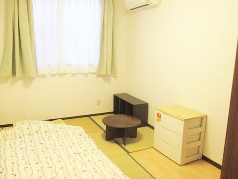 和室タイプの居室である。エアコンや照明が完備されている。畳に布団が敷かれており、壁際にチェストや小さなちゃぶ台が置かれている。