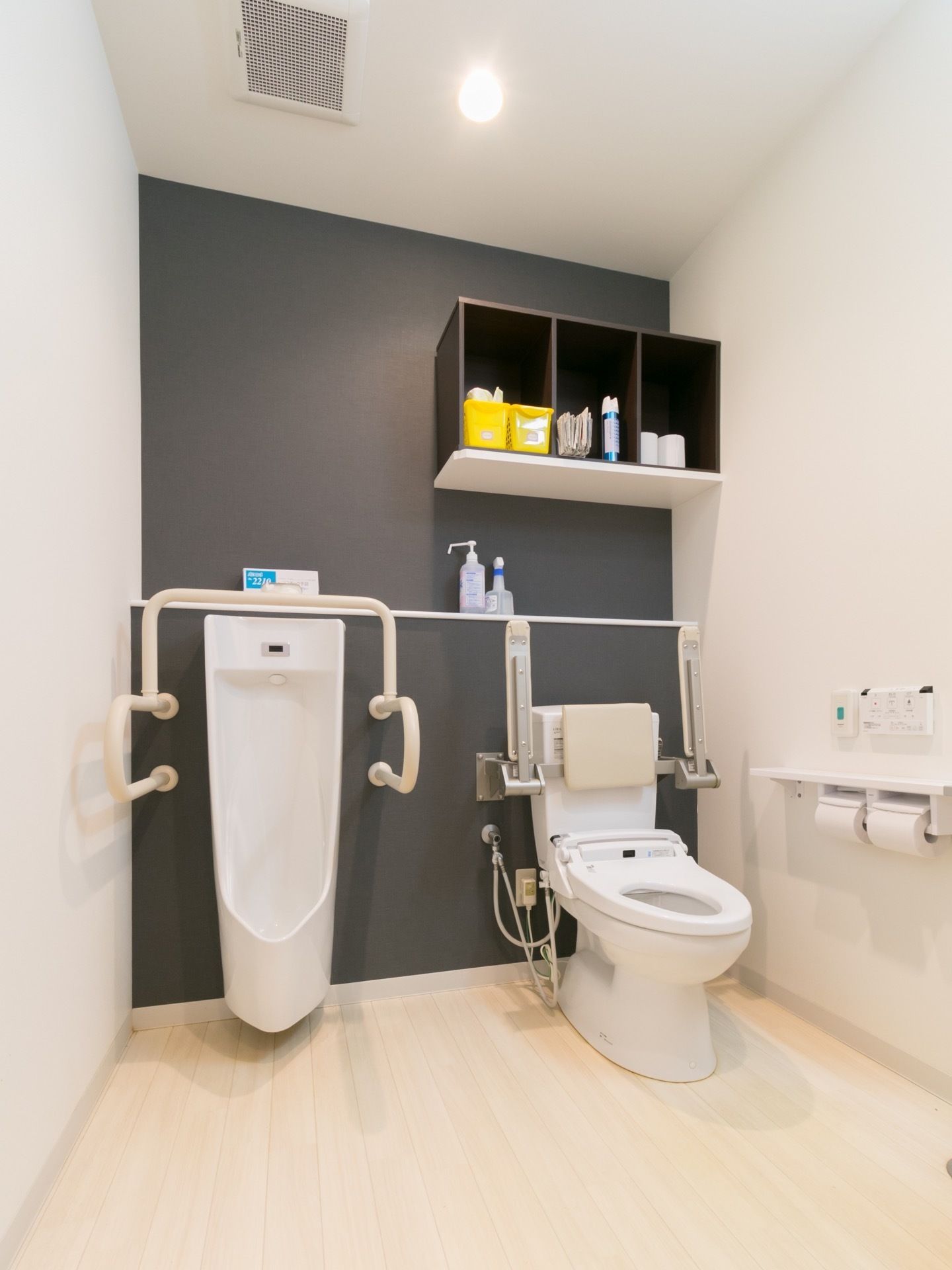 広くスペースを確保したトイレである。男性用小便器や温水洗浄便座器を完備している。手すりや背もたれパッドも設置し安全である。