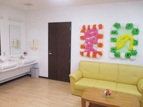 左に洗面台、右に黄土色のソファとテーブル、壁に「愛」や「の」と書いた掲示物のあるスペース