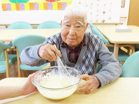 ボウルに入ったクリームのようなものを泡だて器でかき混ぜている高齢男性