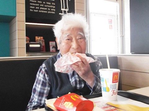 ハンバーガーショップで、ポテトやドリンクとのセットを前にしてハンバーガーをかじっている高齢者