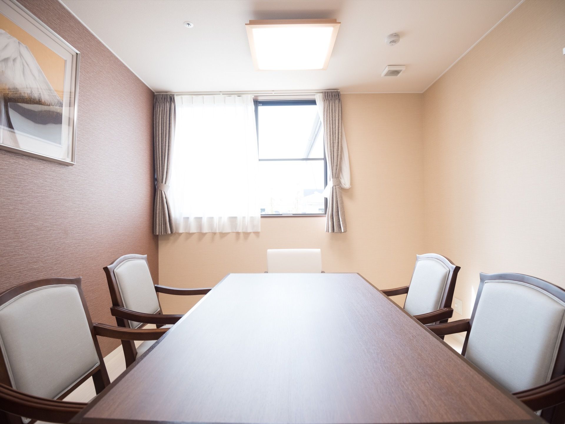 談話室には落ち着いた色合いの木目調の細長いテーブルが設置されていて、背もたれと肘掛けのついた白い椅子がセットされている。