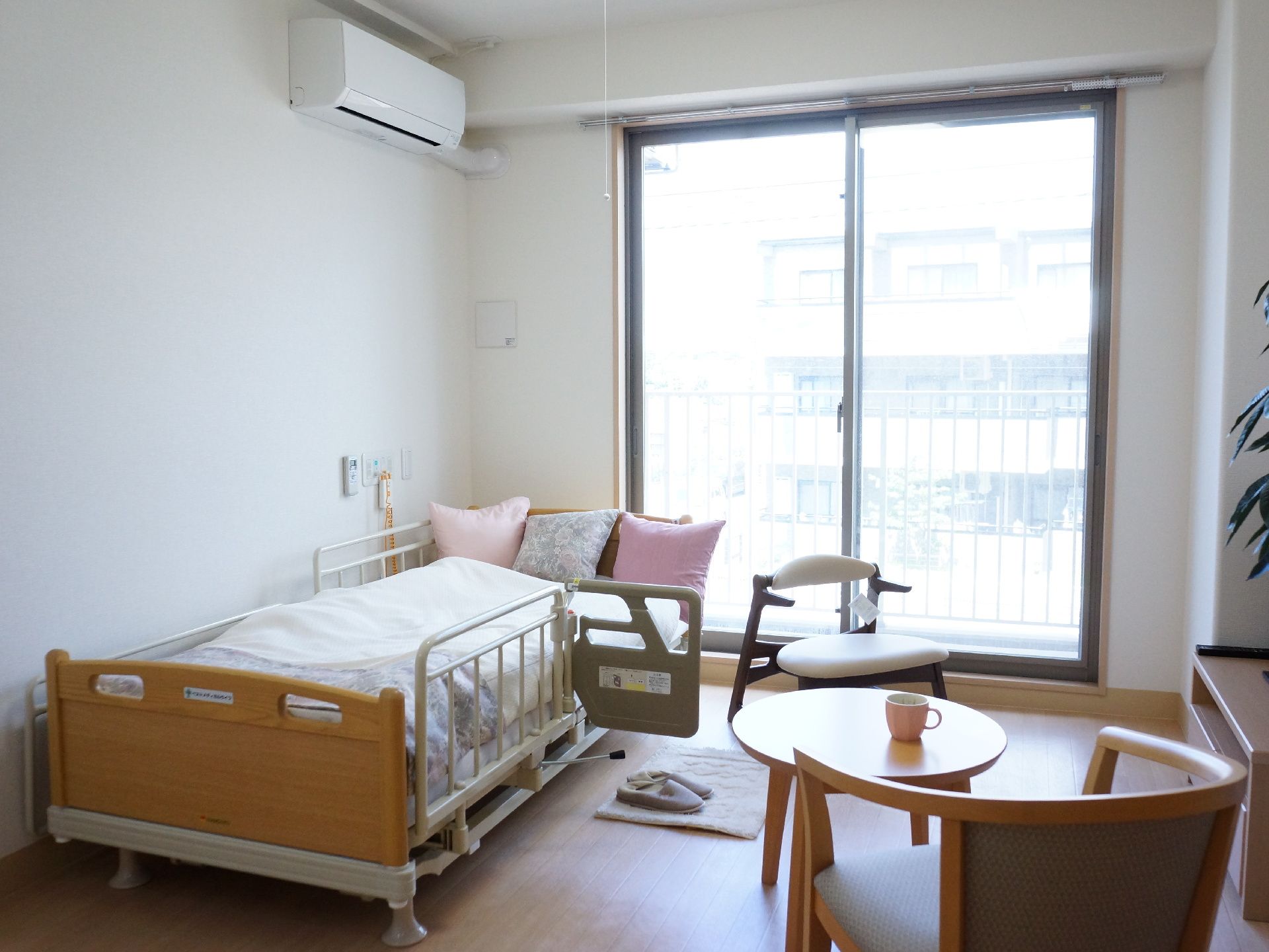 居室の窓の近くに、ベッドが設置されている。ベッドには柵がついていて、一部横に開くようになっている。ベッド横にテーブルと椅子が2脚ある。