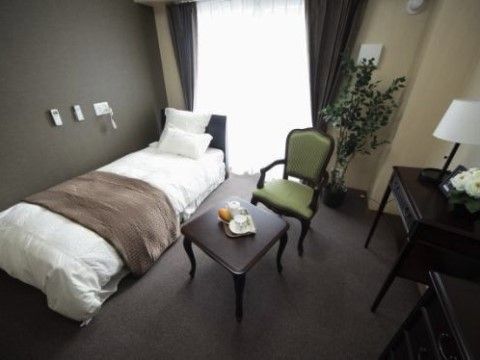 窓辺にベッドとグリーン、中央にテーブルと椅子を配置した居室