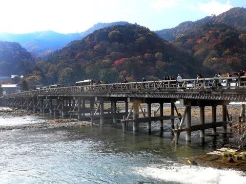 紅葉が始まった山並みと、穏やかに流れる河。そこにかけられた情緒ある橋の上には、行き交う多くの観光客の姿がある。